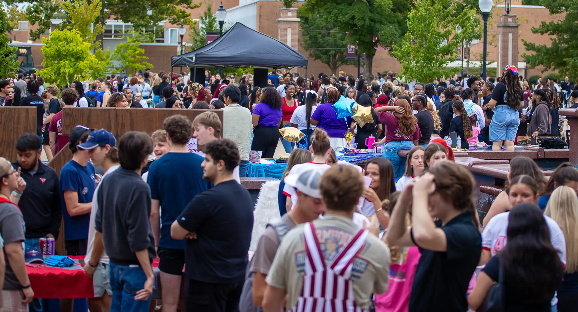 Students gather at a crowded outdoor campus event with tables, tents, and activities.