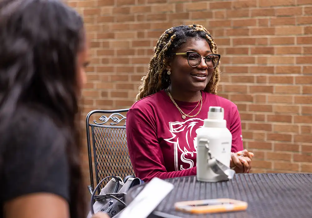 A student in an SIU shirt talks with another student at an outdoor table.