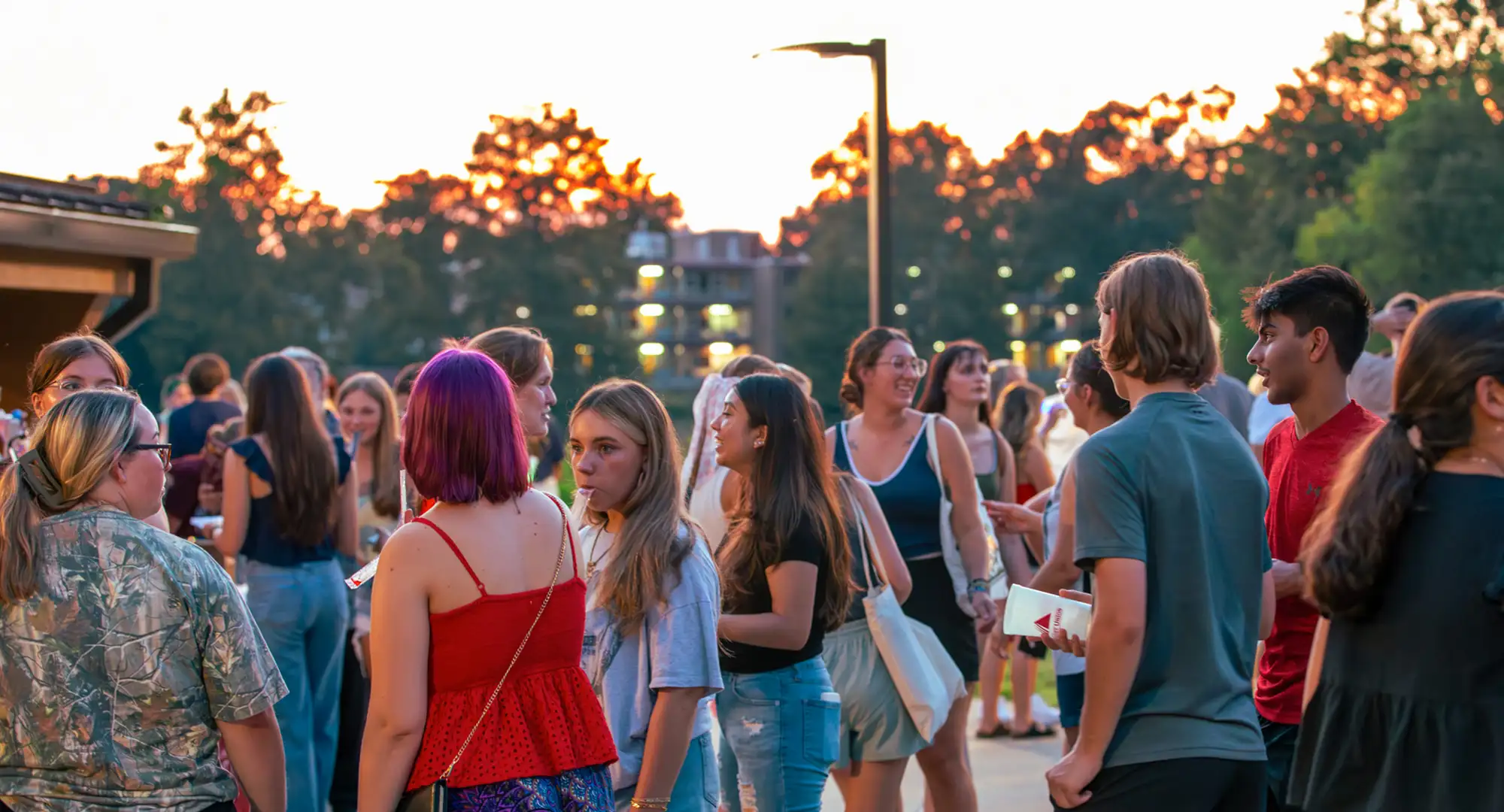 Students gather outdoors at sunset during a campus event.