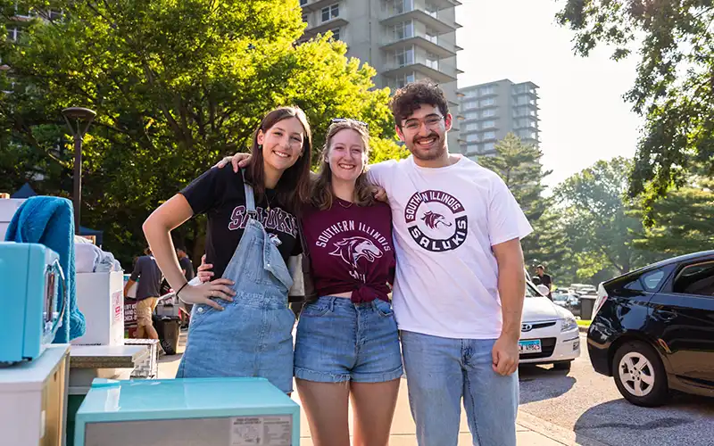 Students smile and pose together outside during move-in with residence towers in the background.