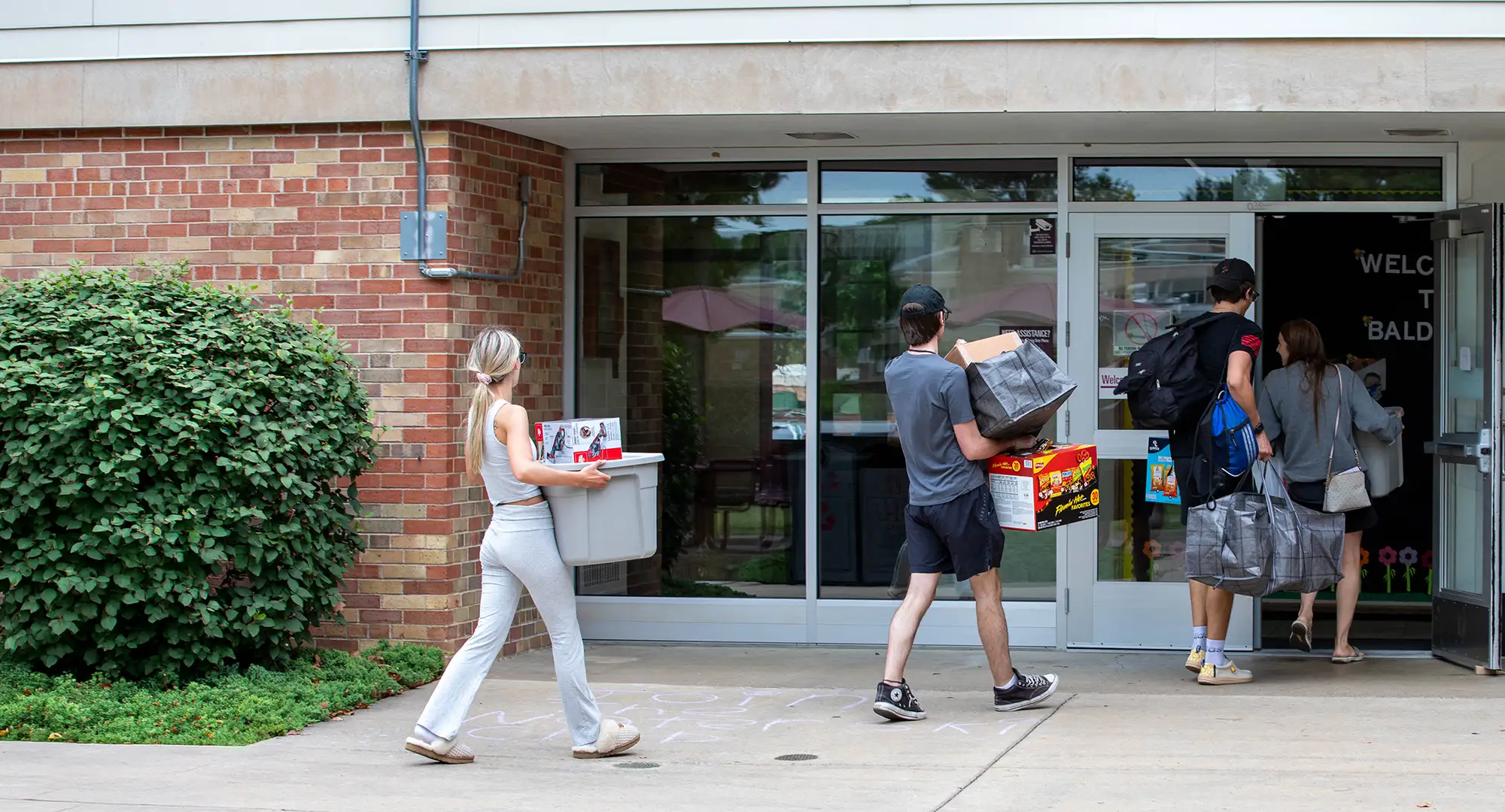 Students carrying bins, bags, and boxes walk into a residence hall during move-in at SIU.