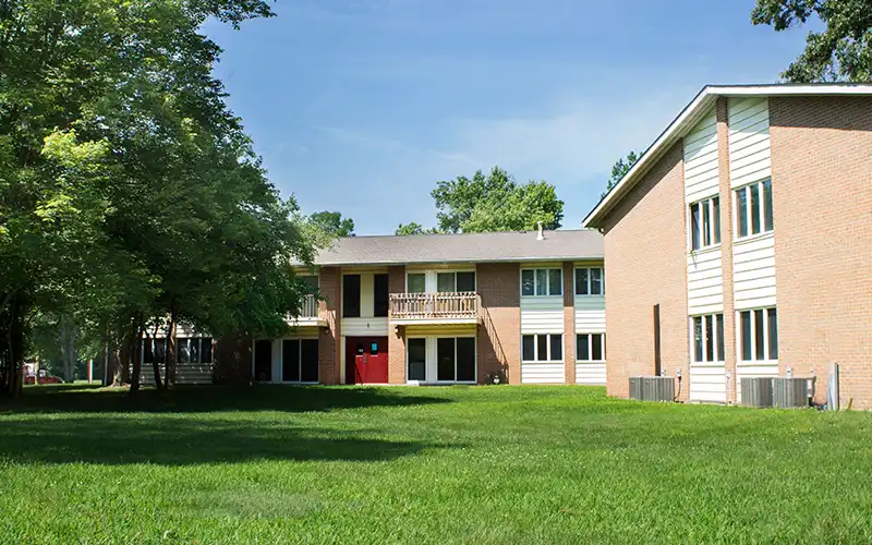 Evergreen Terrace apartment buildings surrounded by large trees and an open grassy lawn under a clear blue sky.