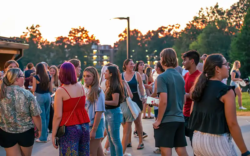 Students gather outside near Thompson Point’s lake and residence halls during a sunset event.