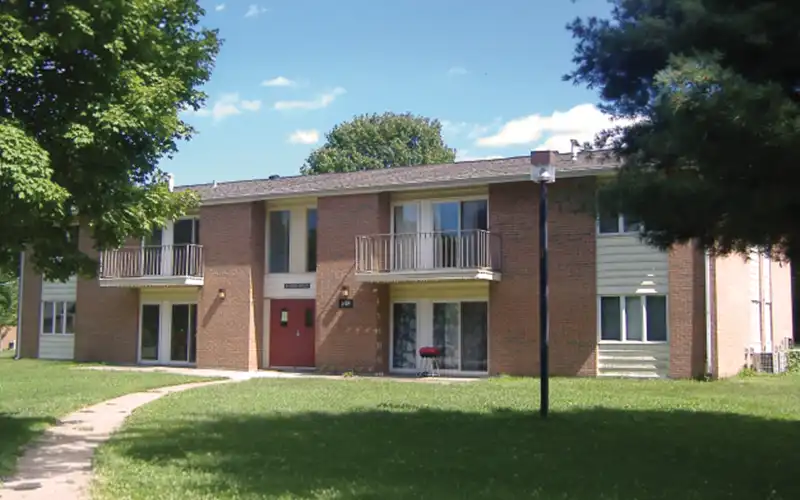 Two-story Evergreen Terrace apartment building with brick exterior, small balconies, and a grassy lawn with surrounding trees.