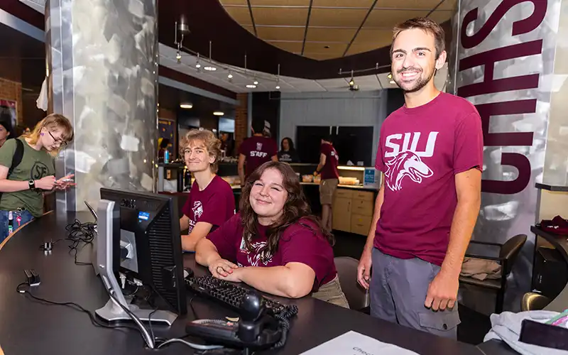 Student staff at a residence hall front desk smiling and assisting students during move-in.