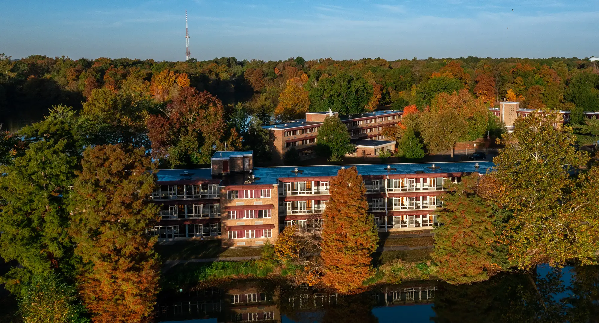 Aerial view of Thompson Point residence halls surrounded by fall foliage, with buildings reflected in the lake below.