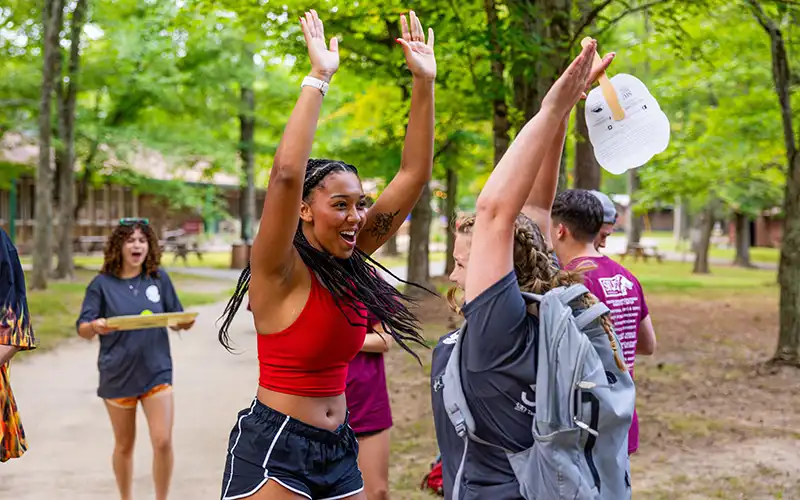 Two students outdoors give each other an excited high-five during a campus event.